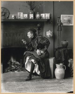 Women Behaving Badly: 400 Years of Power and Protest: Frances Benjamin Johnston.Frances Benjamin Johnston full-length portrait, seated in front of a fireplace, facing left, holding cigarette in one hand and a beer stein in the other, in her Washington DC studio. 1896.