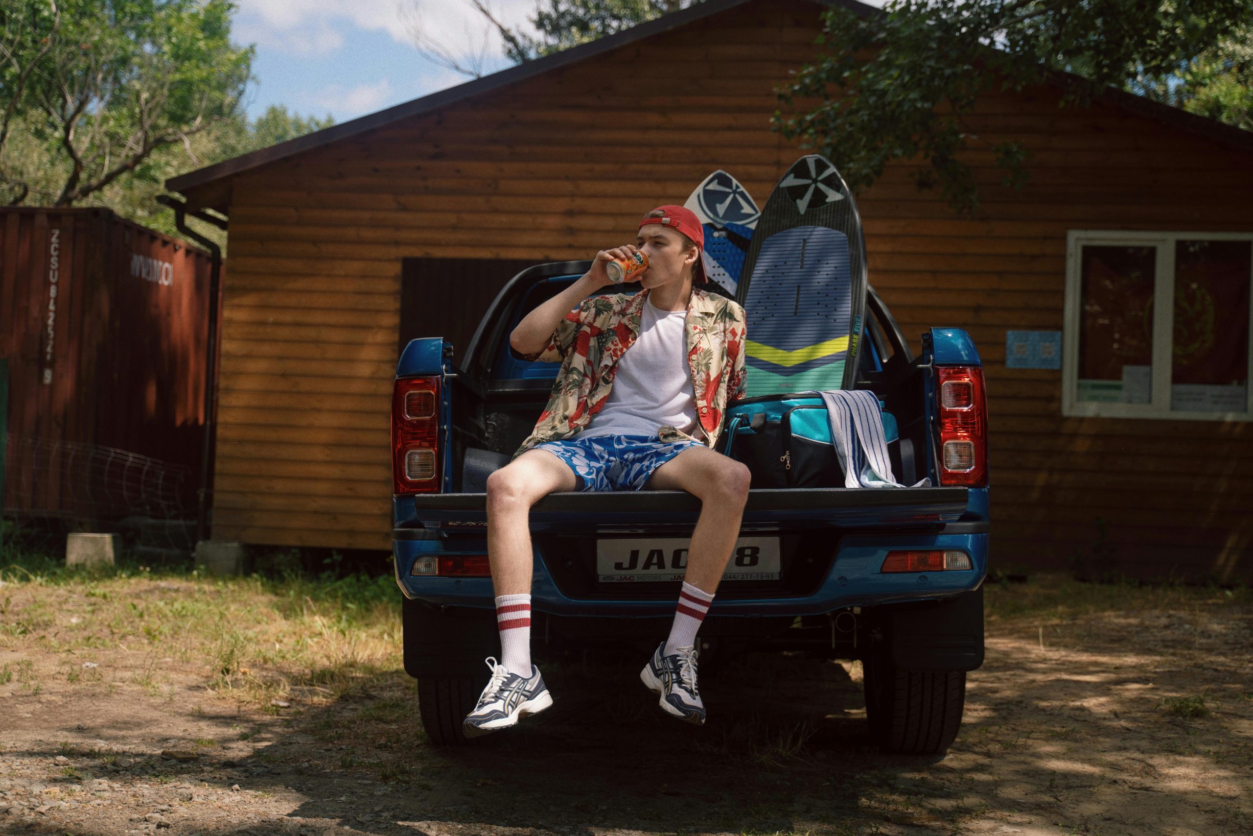 Teeanage Boy Sitting on Car Trunk and Drinking Mirinda