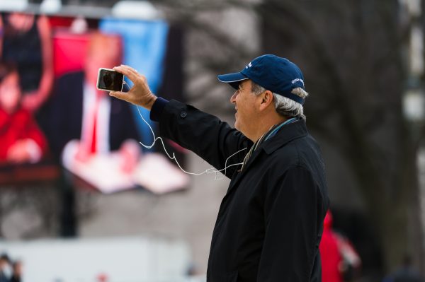 Inauguration Day: "The digital age" A man uses his smart phone to live stream or video call from the National Mall moments after the Inauguration of President Trump. In the background President Trump signs his first executive order. (Michael Jordan)