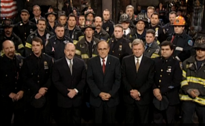 September 29, 2001- Mayor Giuliani stands onstage with members of the NYPD and NYFD (screenshot from NBC.com)